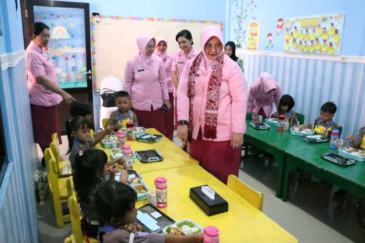 Ketua Bhayangkari Jatim Ny. Ade Imam Sugianto didampingi Ny. Andani Daniel S Marunduri memperhatikan keceriaan anak-anak dapat makan bergizi gratis. (ist)