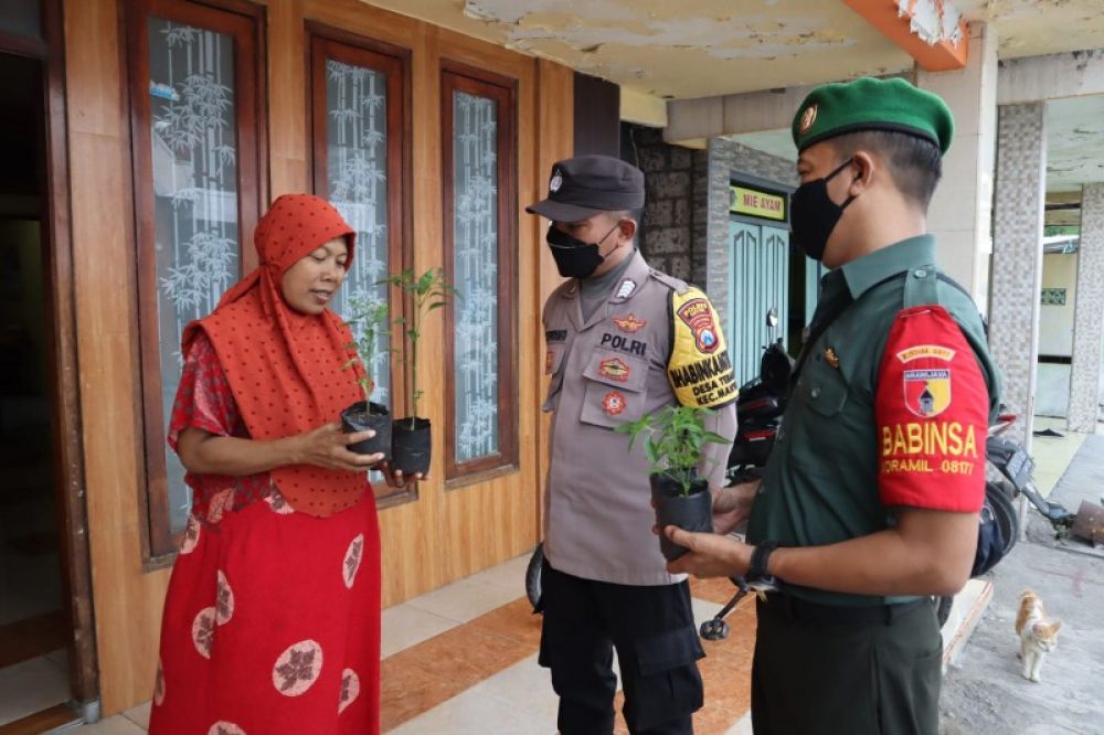 Polsek Manyar Bropka Hadi didampingi mitra kerjanya Serda Triyanto Babinsa Koramil 0817/06 saat menyerahkan bantuan bibit cabe kepada warga. (Ist) 