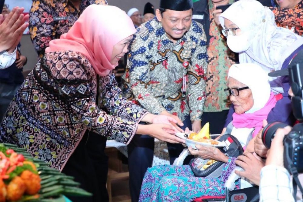 Gubernur Khofifah menyerahkan potongan tumpeng kepada salah seorang ibu lansia jamaah haji saat menyambut kedatangan kloter 87. (Ist) 
